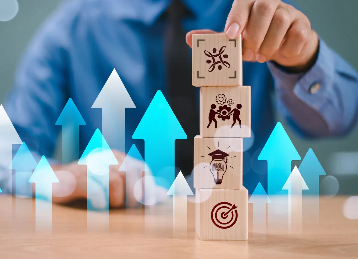 Bloques con íconos de equipo, aprendizaje y objetivos apilados sobre flechas de crecimiento